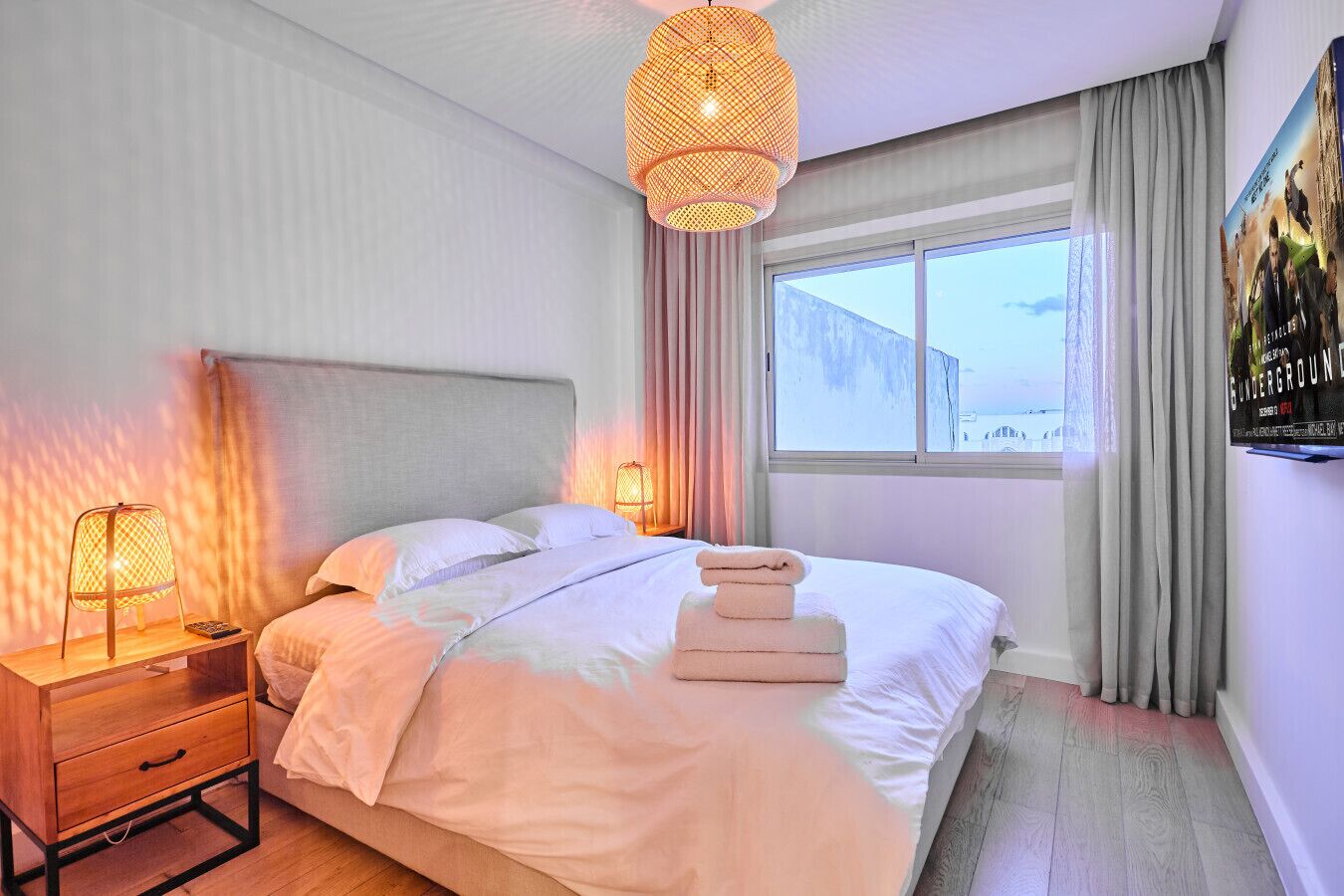 Ein Hotelzimmer mit Bett, Nachttischlampen, einem Fenster mit Vorhängen und einem Poster an der Wand.