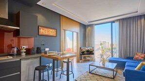 Un salon moderne avec un canapé bleu, une table basse et un coin cuisine équipé d’une cuisinière et de tabourets.