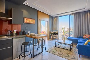 Een moderne woonkamer met een blauwe bank, een salontafel, en een keukenhoek met een fornuis en krukken.