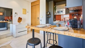 Une cuisine moderne équipée d’un four à micro-ondes, d’une cuisinière et d’une machine à café. On y trouve une porte en bois et un comptoir blanc avec des tabourets.