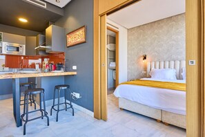 Een moderne hotelkamer met een bed, een kitchenette en een badkamer, zichtbaar door een open deur.