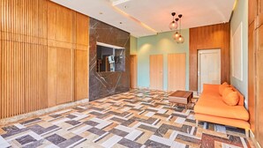 Une chambre d’hôtel avec un parquet à motifs chevrons, des murs lambrissés, un canapé avec des coussins orange et un luminaire suspendu.