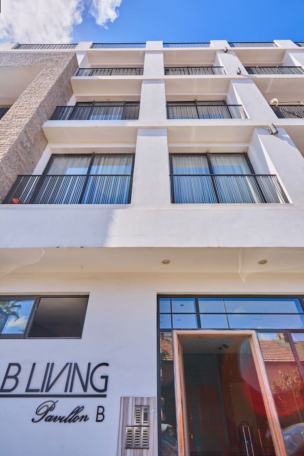 Un edificio de varios pisos con fachada blanca, ventanas grandes y un letrero que dice 'BLIVING Pavillon B'.