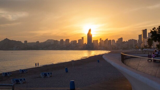 A waterfront promenade with a city skyline in the background during sunset.