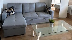 A modern living room with a grey sectional sofa, a glass coffee table, a large mirror, and a hanging woven light fixture.