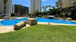 A swimming pool with a grassy area, palm trees, and a view of tall buildings in the background.