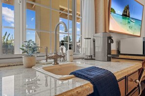 A kitchen with a sink, a potted plant, a towel, and a large window with a view of a beach. - Bella Notte, a ZenStay Hotel - Studio 9 (Pleasure Point)