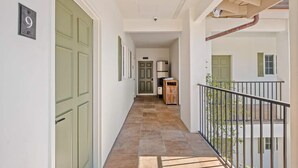 Un corridoio con porte verdi, una zona cucina e un balcone con ringhiera.