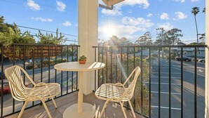 A balcony with two chairs and a table, overlooking a street with cars and trees. - Bella Notte by the beach Studio 8 (Pleasure Point)