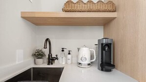 A modern kitchen with a built-in sink, a coffee maker, and a basket on a wooden shelf. - Bella Notte by the beach Studio 7 (Pleasure Point)