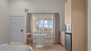 A compact room with a bed, a small dining table with chairs, a kitchenette with a microwave, and a window with curtains. - Bella Notte by the beach Studio 7 (Pleasure Point)