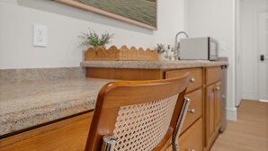 Une cuisine avec une chaise en bois, un four à micro-ondes et une vue sur la plage, visible par une fenêtre.