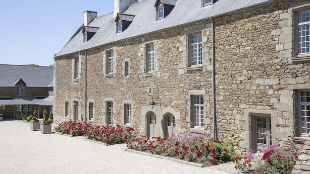 A stone building with multiple windows and a courtyard with flowers. - Hotel de l Abbaye Le Tronchet Saint Malo (Le Tronchet)