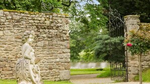 A stone wall with a statue, a metal gate, and a pathway leading to a body of water. - Hotel de l Abbaye Le Tronchet Saint Malo (Le Tronchet)