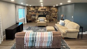 Una sala de estar con pared de piedra, chimenea, sofá, sillón y televisor.