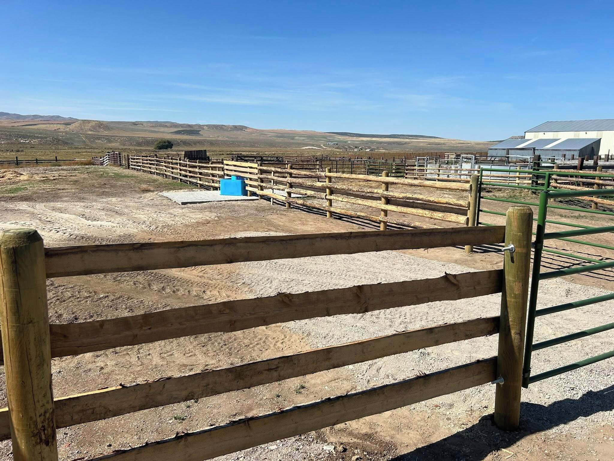 A fenced outdoor area with a dirt ground, wooden fence posts, and a blue container.