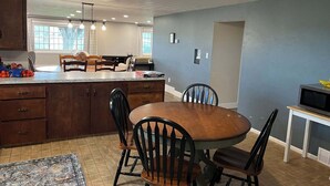 Una cocina con mesa, sillas, armarios y un microondas.