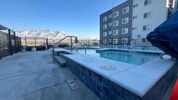 A rooftop pool with a view of mountains, a building with multiple windows, and a blue-tiled edge.