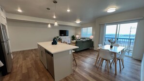Une cuisine moderne dotée d’un îlot central, d’un coin repas avec une table et des chaises, et d’une grande fenêtre offrant une vue dégagée.