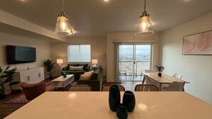 Un salon moderne avec une grande table blanche, un canapé, un téléviseur et un balcon offrant une vue dégagée.