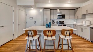 Una cocina moderna con una isla central, taburetes de bar y un microondas.