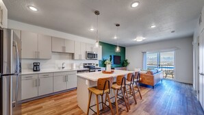 Uma cozinha moderna com uma ilha central, banquetas e um espaço de refeições com sofá e vista para o exterior.
