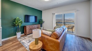 Uma sala de estar com um sofá, uma televisão, um armário de madeira e uma vista através de uma grande janela.