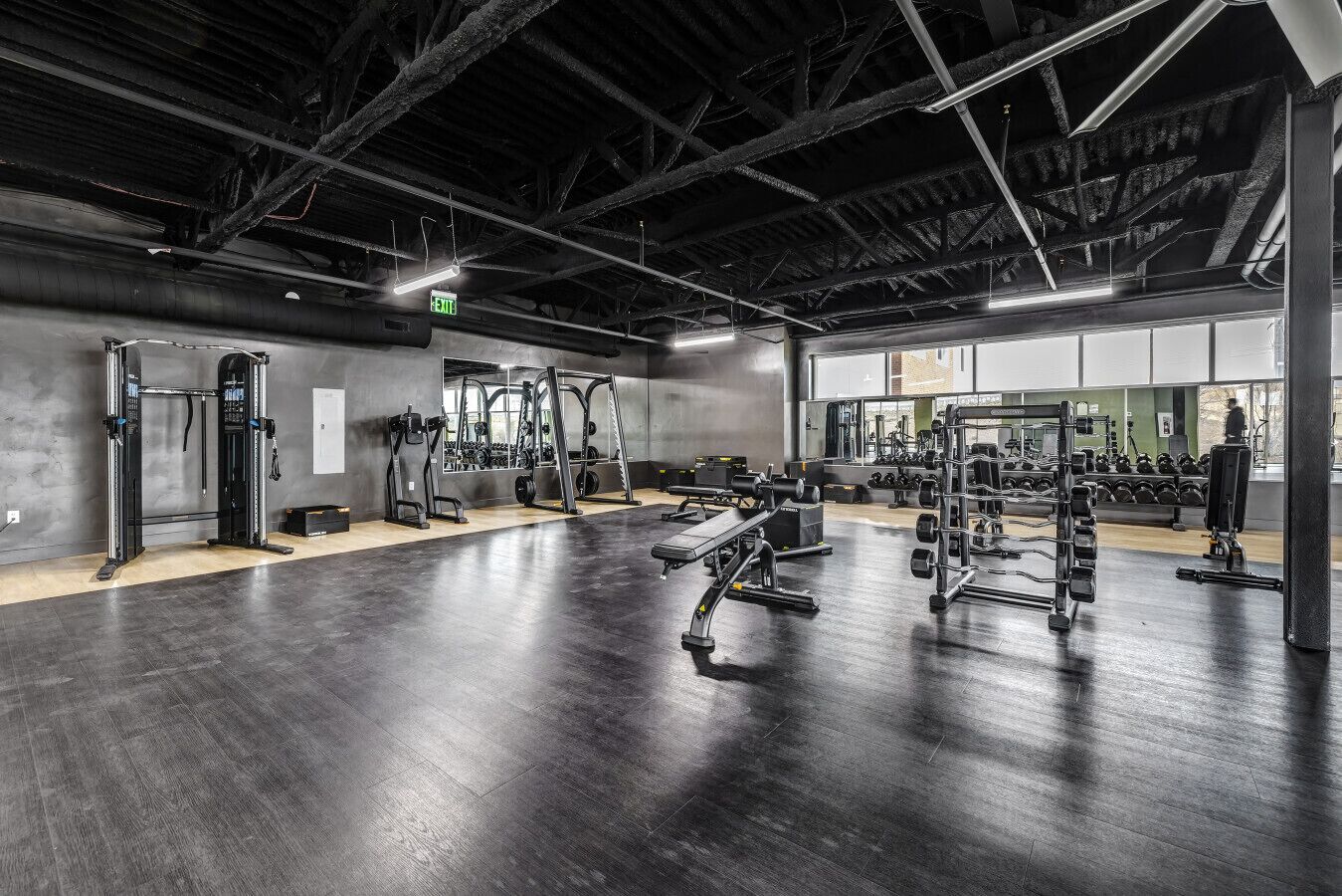 Ett gym med olika typer av styrketräningsutrustning, en vägg med speglar och ett trägolv.