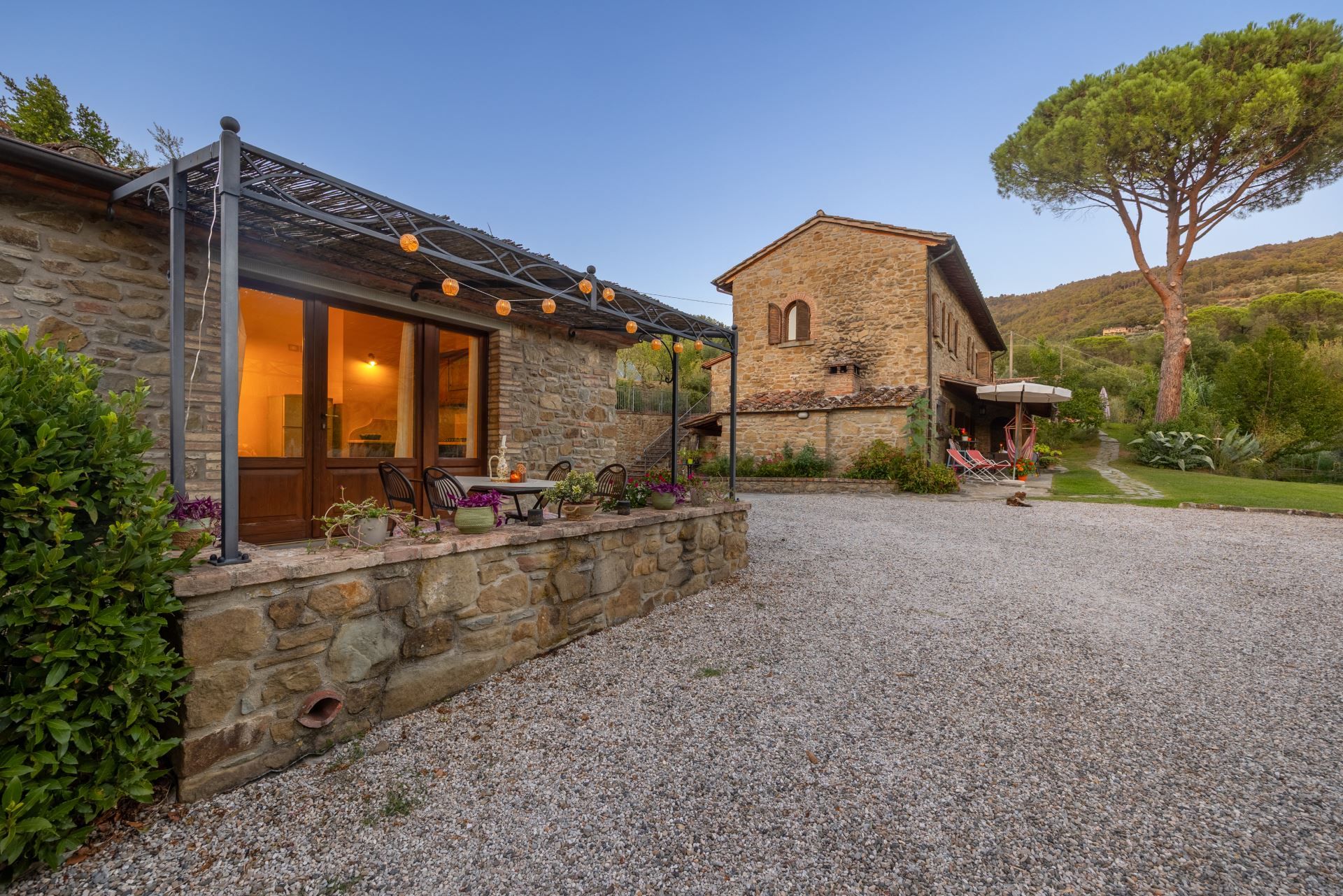 A stone building with a gravel driveway, outdoor seating, and a tree in the background.