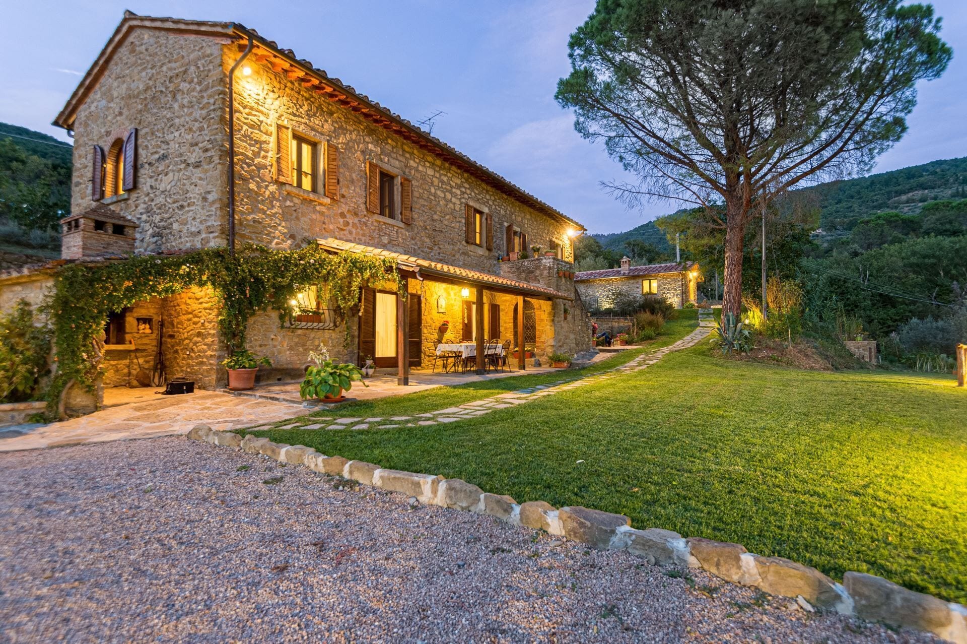 A stone house with a covered patio, a gravel driveway, and a well-maintained lawn.