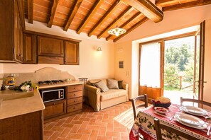 A kitchen with wooden cabinets, a stove, and a dining area with a table set for two. - Agriturismo Antica Quercia Verde - Il Risveglio (Cortona)
