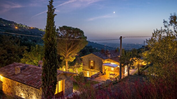 Una casa in pietra con un cortile, circondata da alberi e colline.
