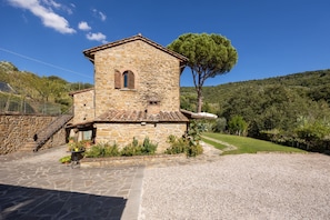 A stone building with a small window and a door, surrounded by a gravel driveway and a grassy area. - Agriturismo Antica Quercia Verde - La Fonte (Cortona)