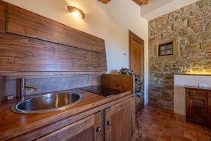 A kitchen with a stainless steel sink, wooden cabinets, and a stone wall. - Agriturismo Antica Quercia Verde - La Fonte (Cortona)