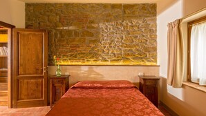 Una camera da letto con parete in pietra, mobili in legno, un letto con copriletto rosso e una finestra con tende.