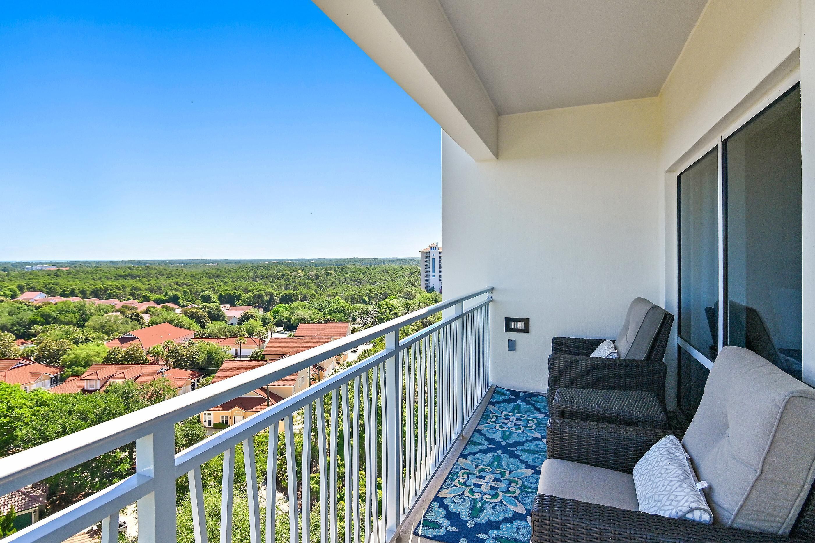 A balcony with a view of a residential area, a wicker sofa, and a patterned floor.