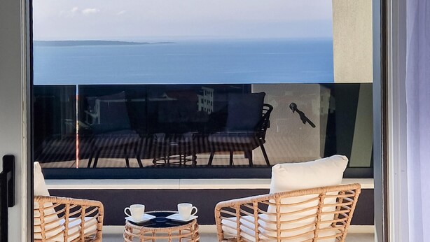 Un balcón con sillas de mimbre y una mesa, con vista a una extensión de agua.