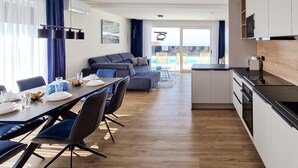 Ein modernes Hotelzimmer mit Essbereich, einer Couch, einer Küche und Blick auf den Pool.