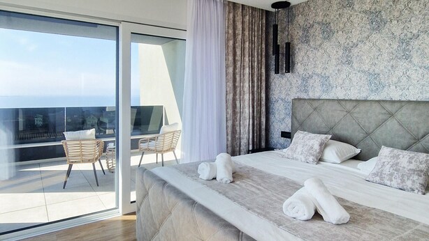 Ein modernes Hotelzimmer mit einem großen Bett, einem Balkon mit Sitzgelegenheiten und Blick auf die Stadt.