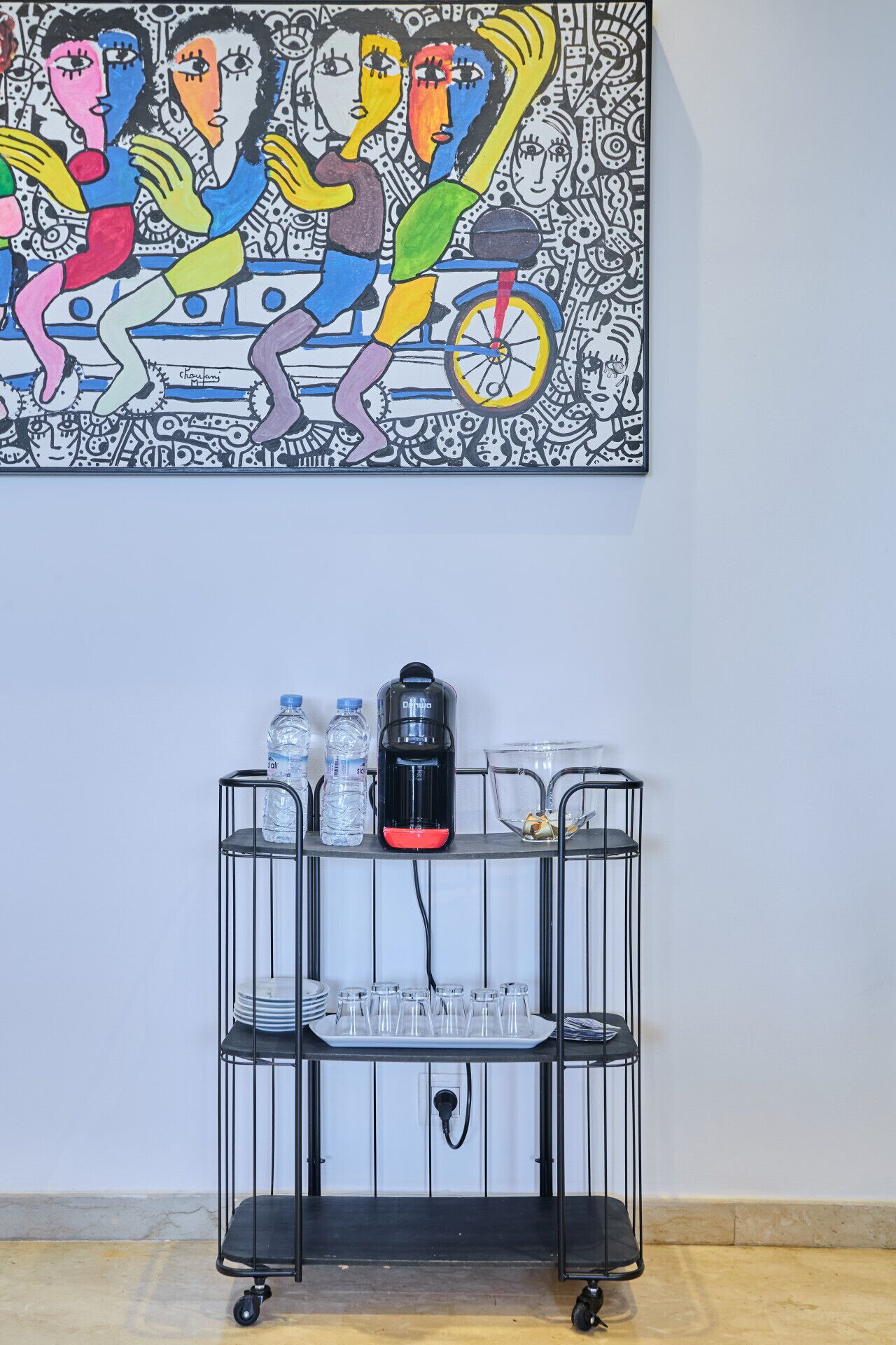 A metal cart with water bottles, a thermos, and glasses on a wall-mounted rack.