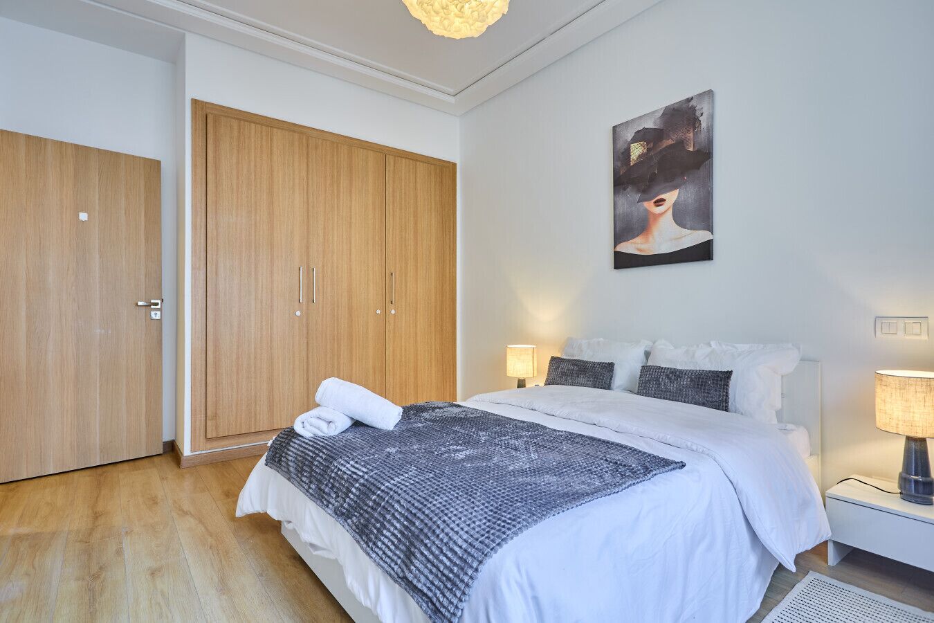 A bedroom with a bed, two bedside tables, a nightstand, a wardrobe, and a painting on the wall.