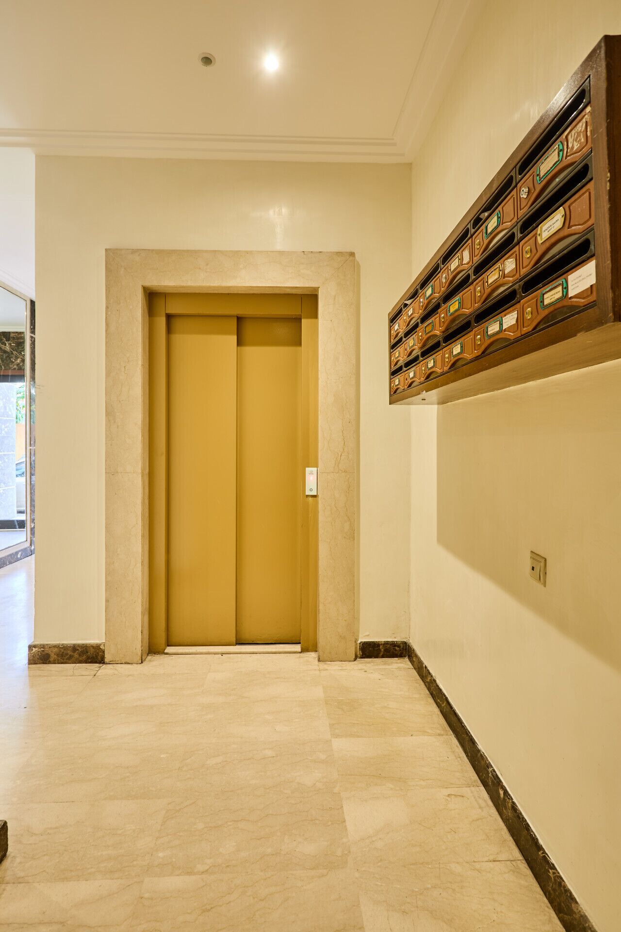 A hallway with a double door, a marble floor, and a wall-mounted storage unit.