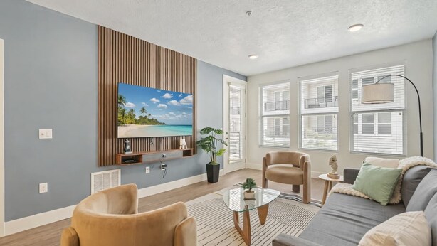 Een woonkamer met een televisie, twee stoelen, een bank, een salontafel en een groot raam met zonwering.