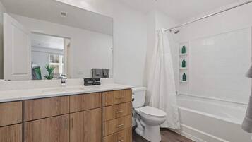Ein modernes Badezimmer mit einem Holzkosmetikschrank, einer weißen Toilette, einer Duschkabine mit Vorhang und einem großen Spiegel.