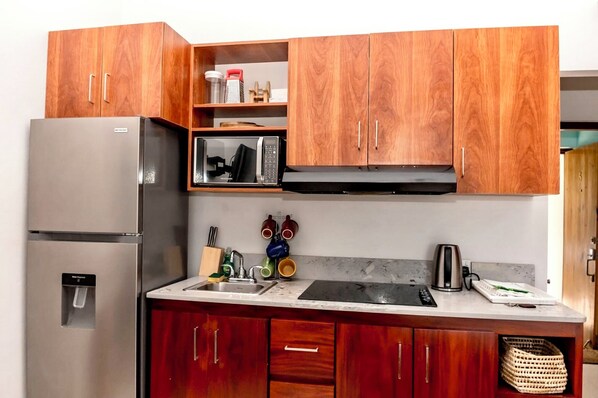 Una cocina con armarios de madera, un refrigerador de acero inoxidable, un microondas y un lavamanos.