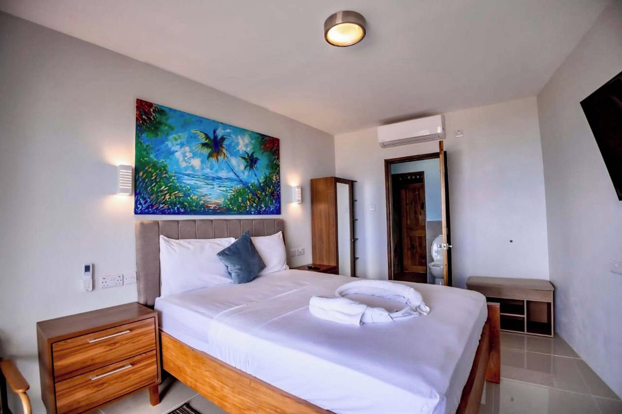 Un dormitorio con cama, mesitas de noche, un cuadro, un equipo de aire acondicionado y un banco.
