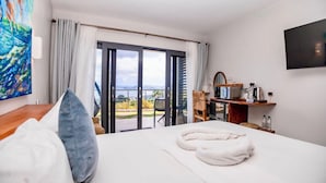 A hotel room with a bed, a TV, a desk with a kettle, and a view of the outdoors. - Hammock Suites MUP - by Zenbreak (Castries)