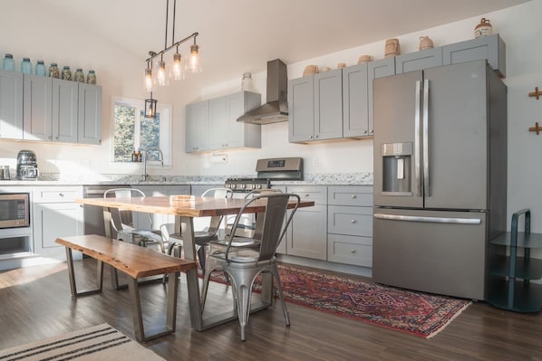 A modern kitchen with a wooden dining table, stainless steel appliances, and light gray cabinetry.