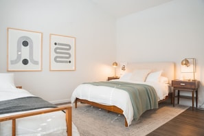 A bedroom with two beds, a nightstand with a lamp, and two framed abstract artworks on the wall.