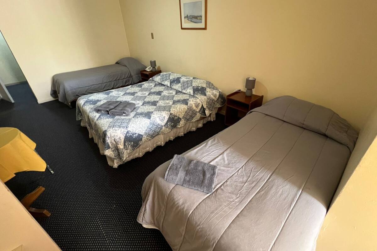 Habitación de hotel con dos camas, una mesita, una silla y un cuadro en la pared.